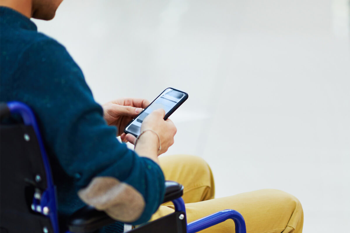 A person sitting in a wheelchair, viewed from behind, looking at a smartphone