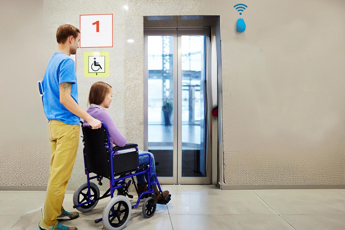 An assisted travel agent pushing a woman in a wheelchair towards an elevator at an airport, with a location beacon visible